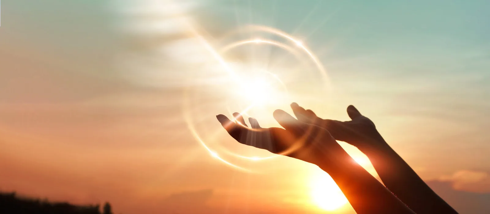 Two silhouetted hands reach upward toward a glowing light with circular lens flare against an orange and blue sunset sky above a dark horizon.