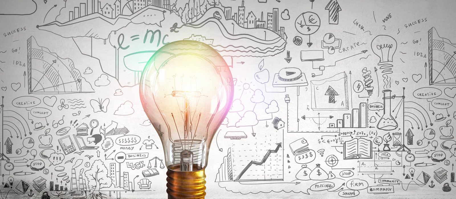 A glowing light bulb in front of a chalkboard wall covered with hand-drawn business and science diagrams.